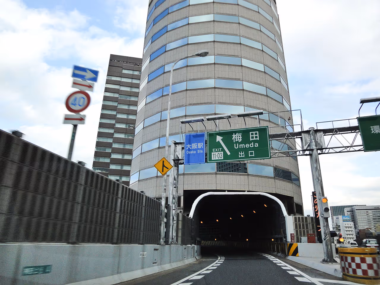 A cylindrical office tower in Japan with a multi-lane expressway passing directly through its fifth to seventh floors.