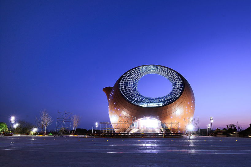 A large building shaped like a traditional Chinese teapot with a circular hollow center and glowing glass panels.