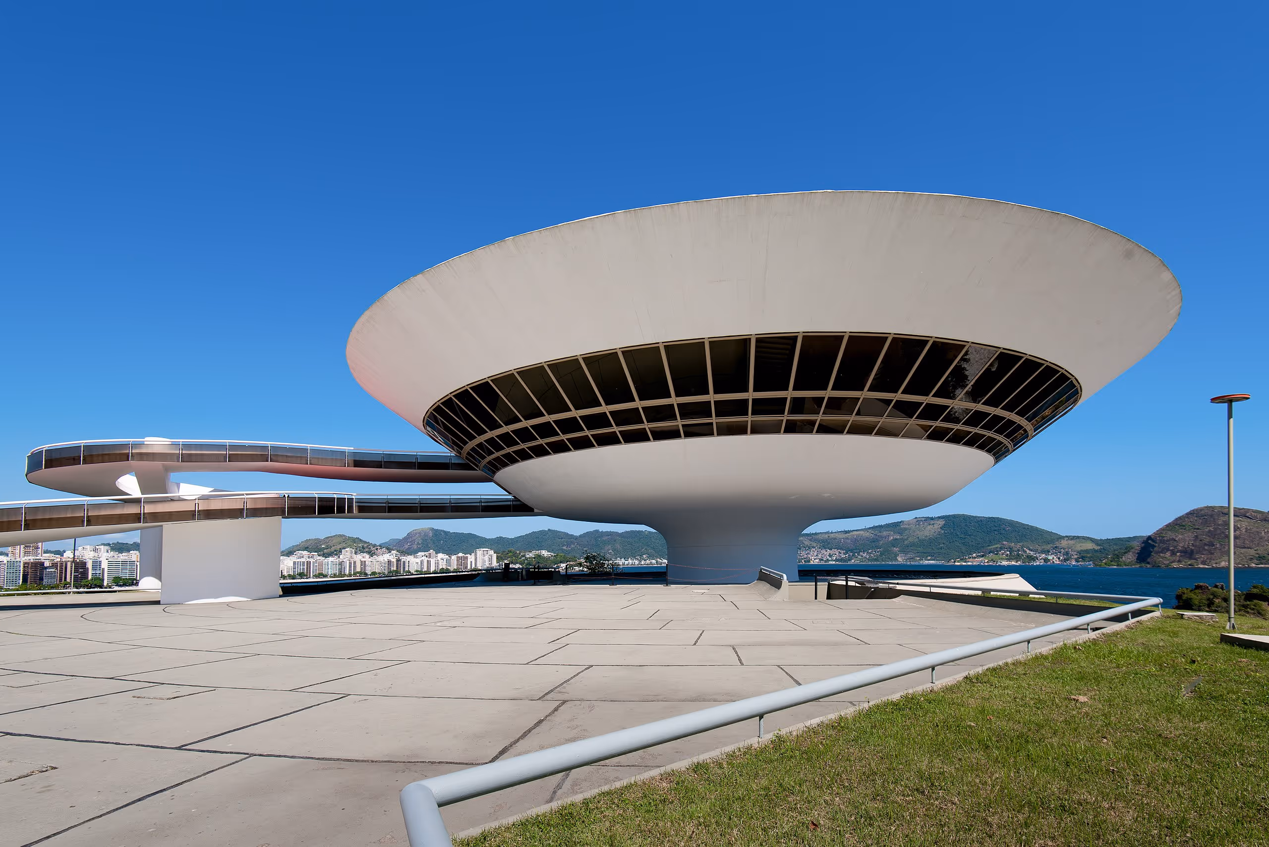 A futuristic white saucer-shaped museum elevated on a narrow base, with a spiral walkway leading up to it.