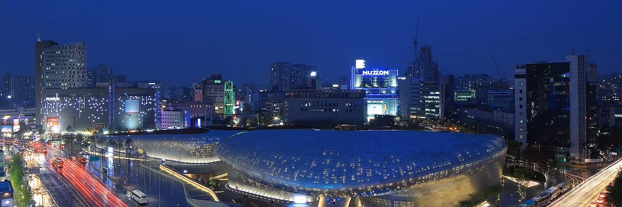 A large silver, spaceship-like complex with curved forms and flowing LED lights, surrounded by a bustling city.
