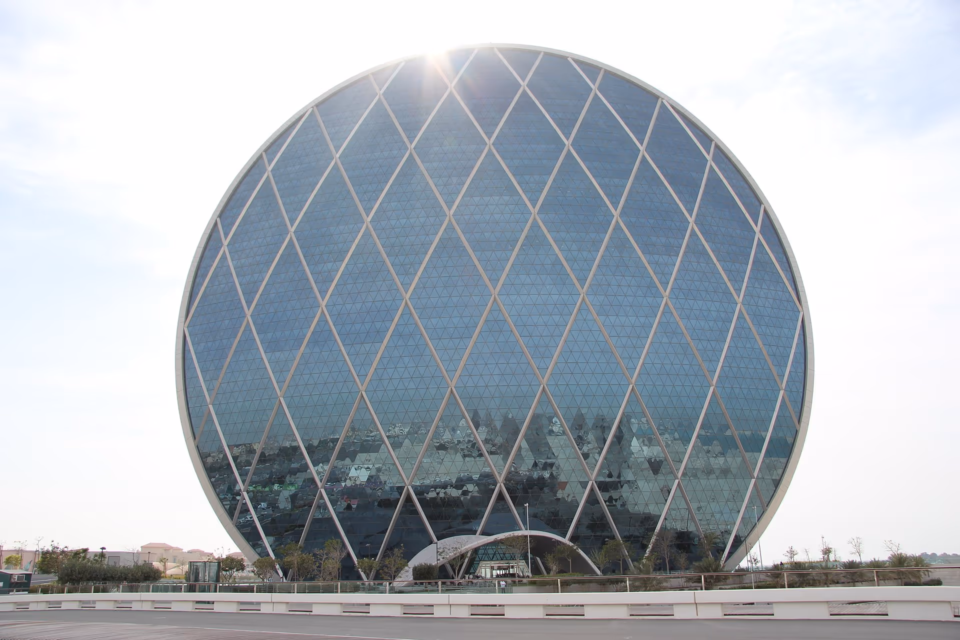 A perfectly round, glass-clad office building with a diamond-patterned steel framework, standing out against the sky.