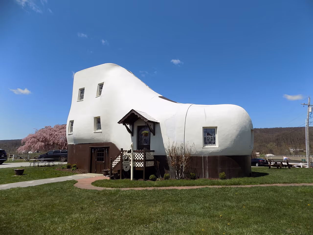 A building shaped like a giant white work boot, with brown trim and small windows, situated in a grassy field.