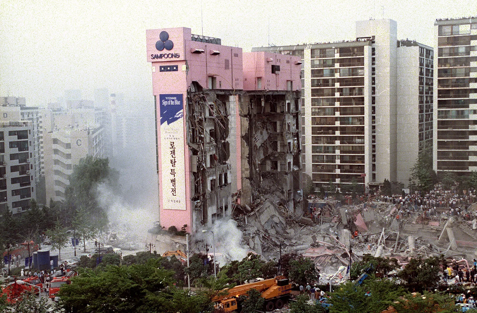 Damaged Sampoong high-rise building surrounded by debris and emergency response crews.