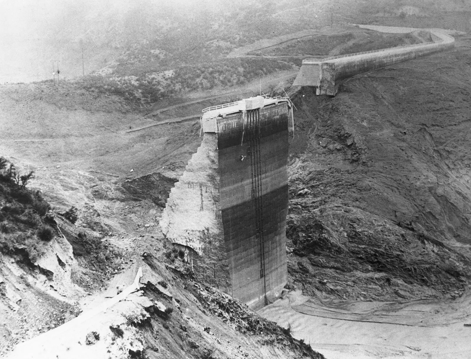 Black-and-white photo of a partially standing St. Francis dam wall in a barren landscape.