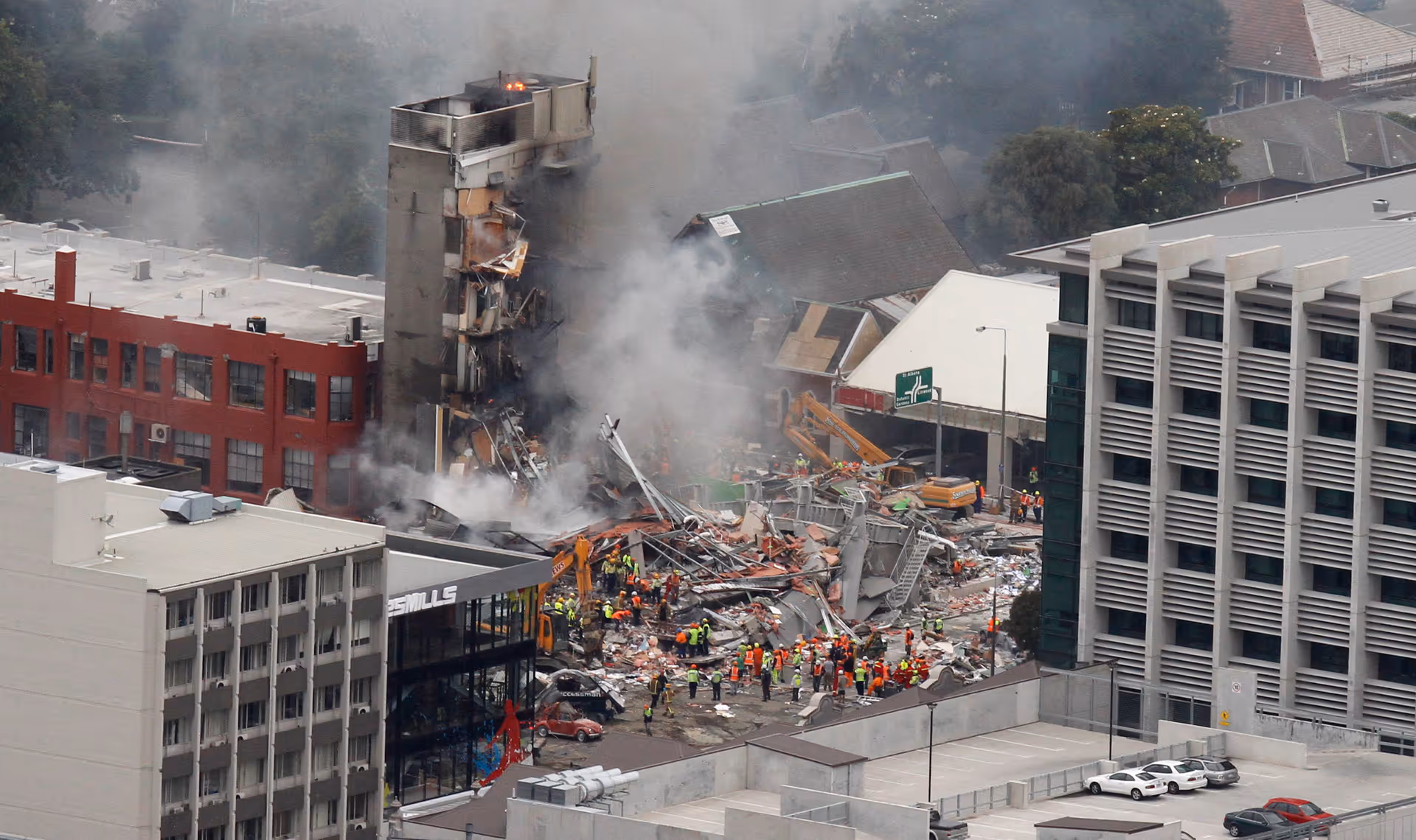 Wreckage and smoke at the CTV Building site with emergency crews clearing debris after the Christchurch earthquake.