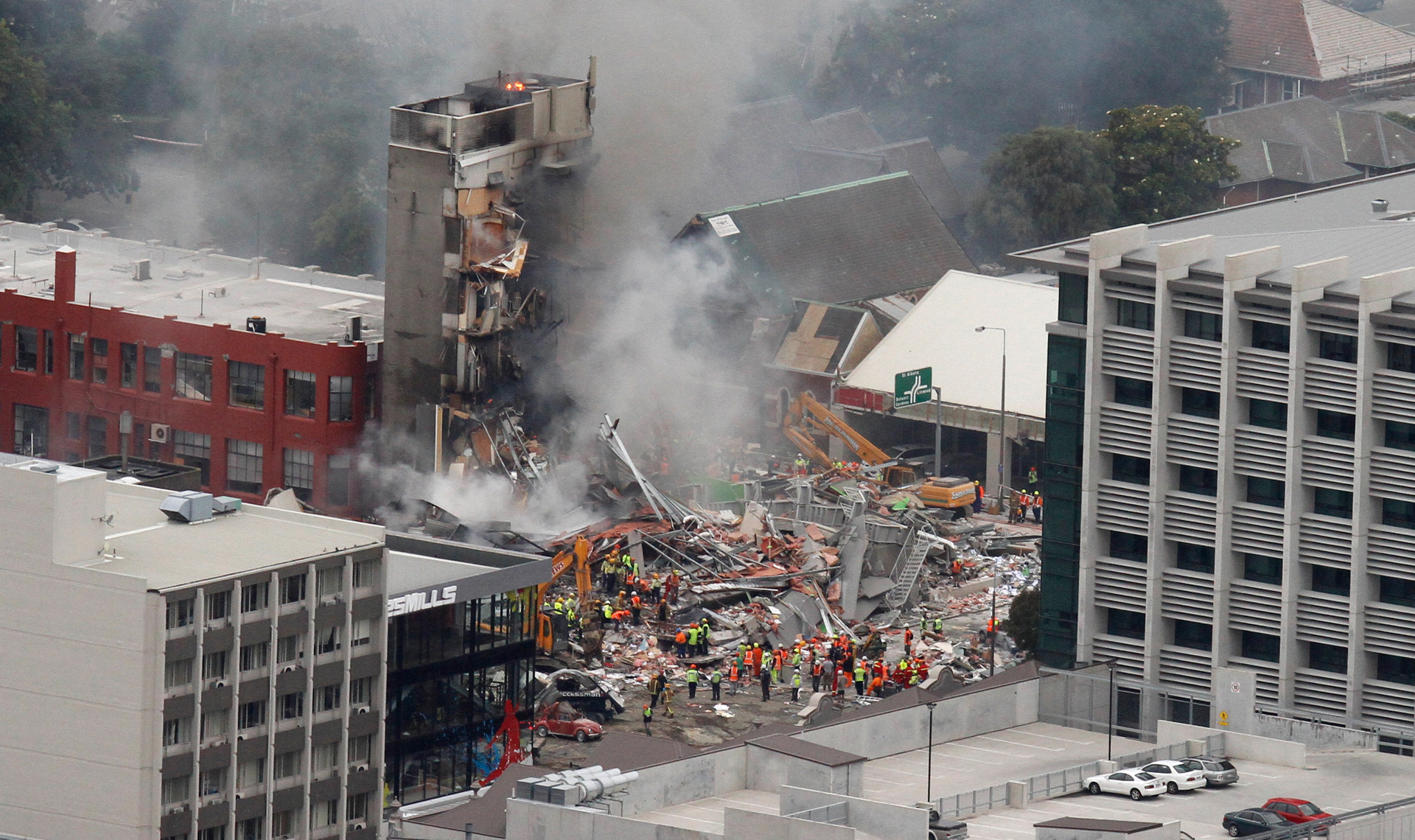Wreckage and smoke at the CTV Building site with emergency crews clearing debris after the Christchurch earthquake.