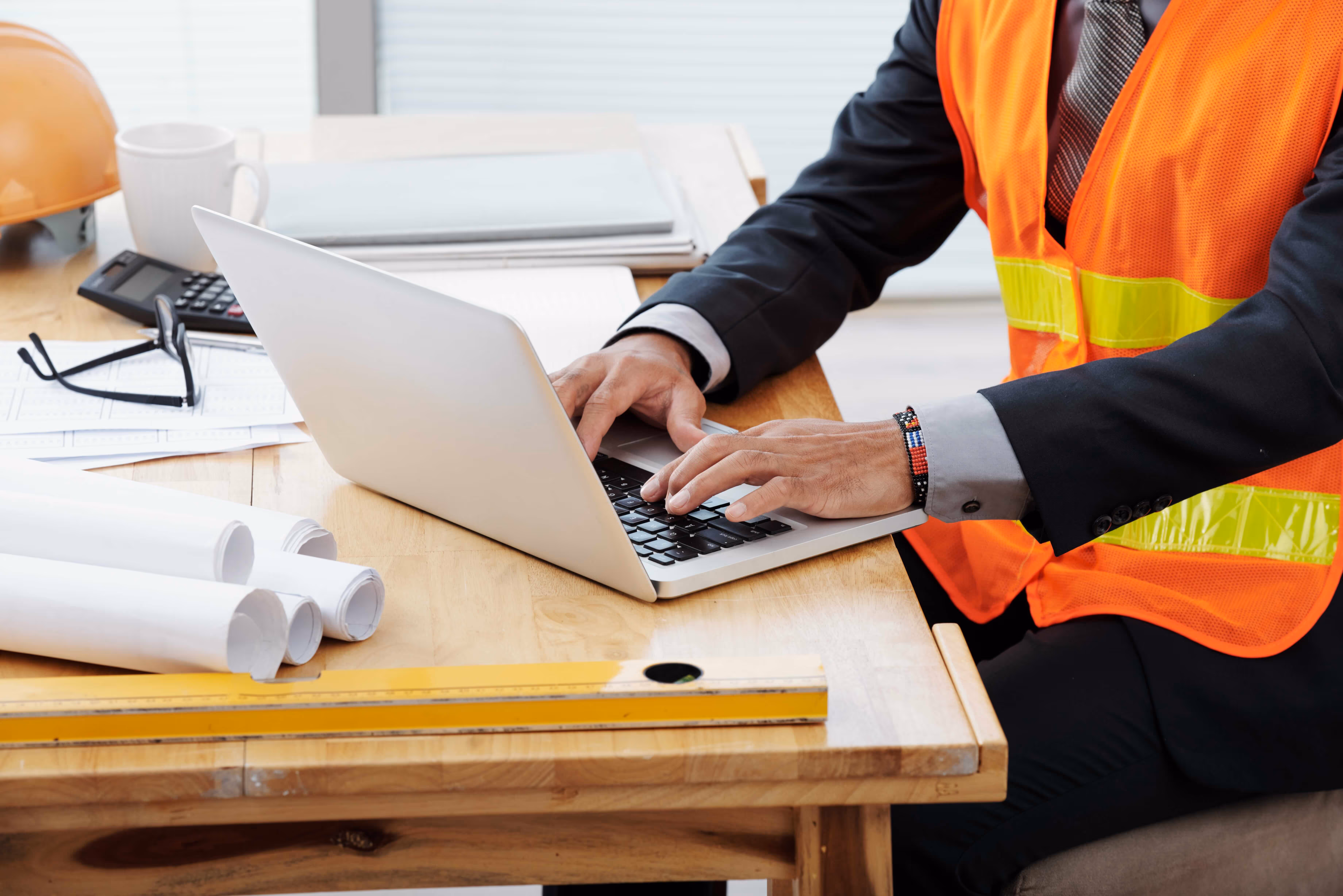 Contractor in safety vest working on a laptop to fill out a continuation sheet for a construction project.
