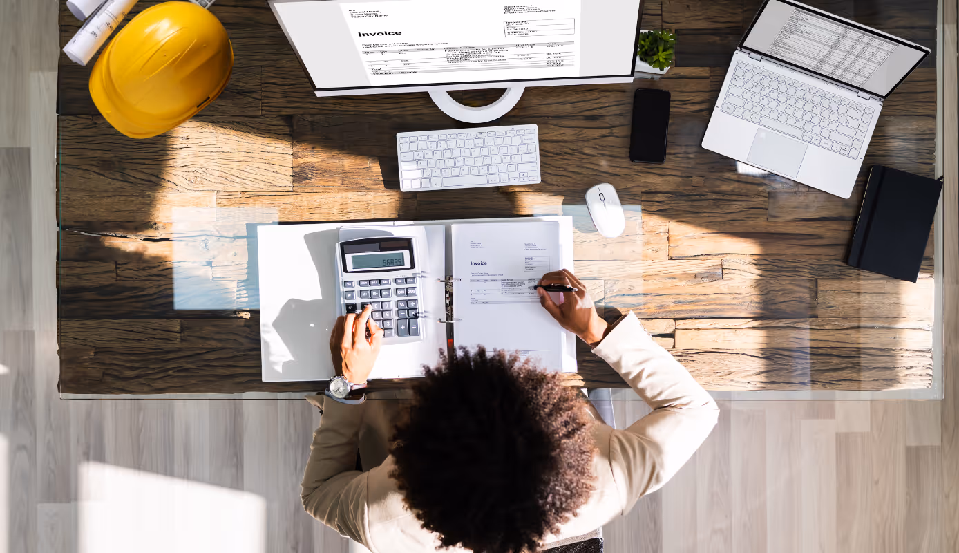 Contractor reviewing project invoices and calculating costs using accounting records on a desk.