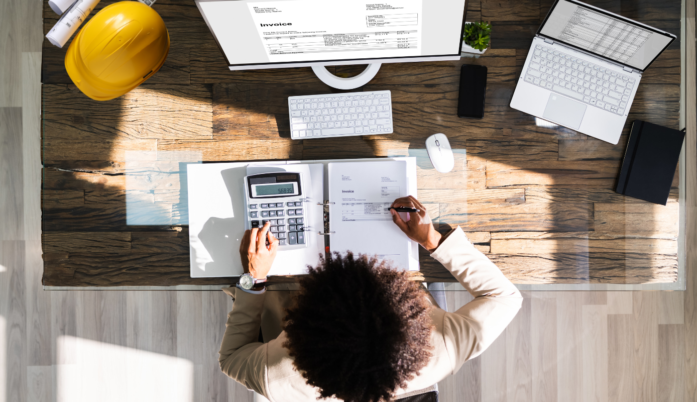 Contractor reviewing project invoices and calculating costs using accounting records on a desk.