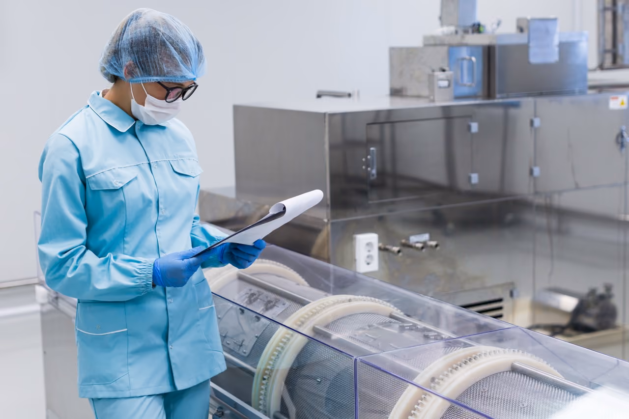 Healthcare worker in protective clothing reviews documents beside sterilization equipment in a hospital CSSD.