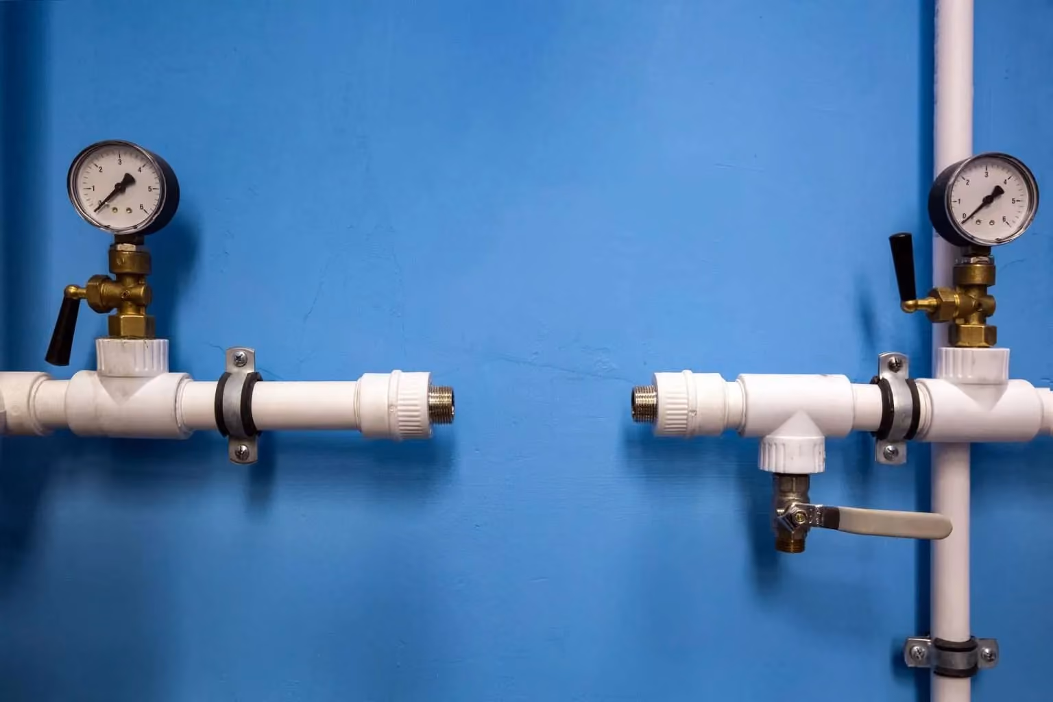 Hospital plumbing pipes with pressure gauges and valve connections against a blue wall.