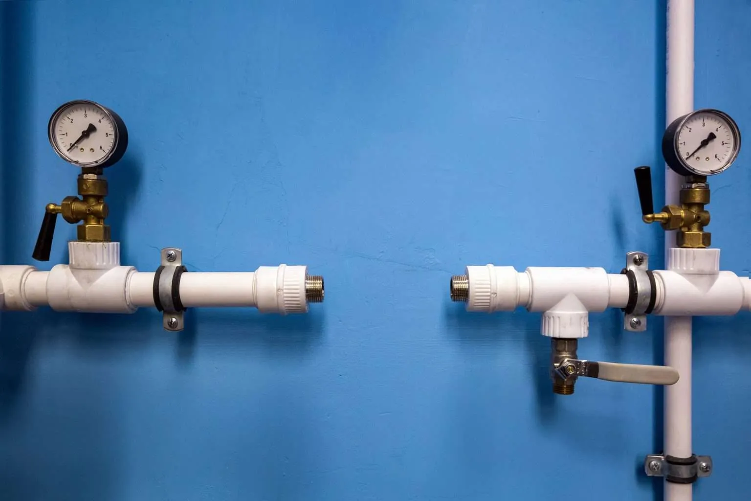 Hospital plumbing pipes with pressure gauges and valve connections against a blue wall.