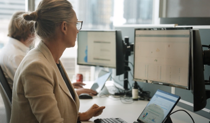 A construction project management professional reviews real-time project data on a large monitor and laptop in a modern office. The screen displays dashboards and analytics, symbolizing efficiency, control, and informed decision-making in capital project management.