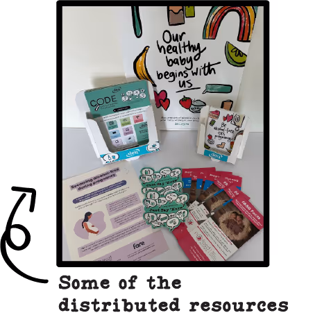 Brightly coloured paper flyers and posters with encouraging messages such as "Our healthy baby begins with us". An arrow points to the photo, reading "Some of the distributed resources".