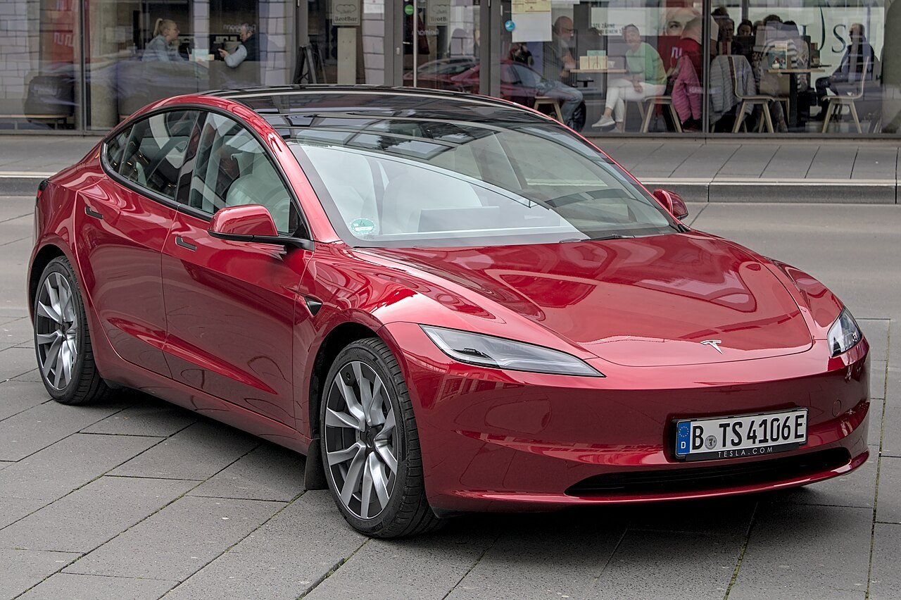 A Tesla Model 3 in red, three-quarter front view on a city street.