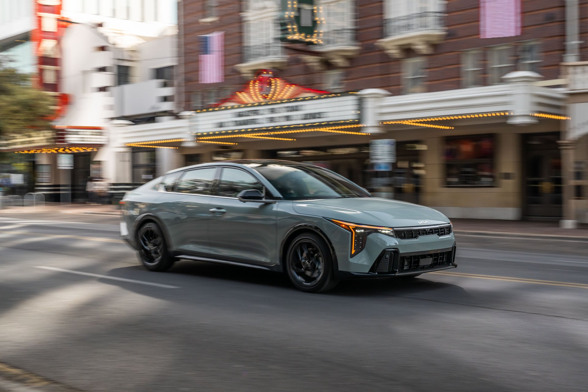 A 2026 Kia K4 sedan in sage green, three-quarter front view on a city street.