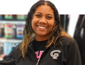 Smiling woman with curly hair wearing a black jacket with a logo, standing indoors.
