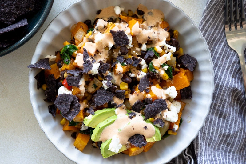 A bowl with roasted butternut squash and other veggies topped with a sauce.