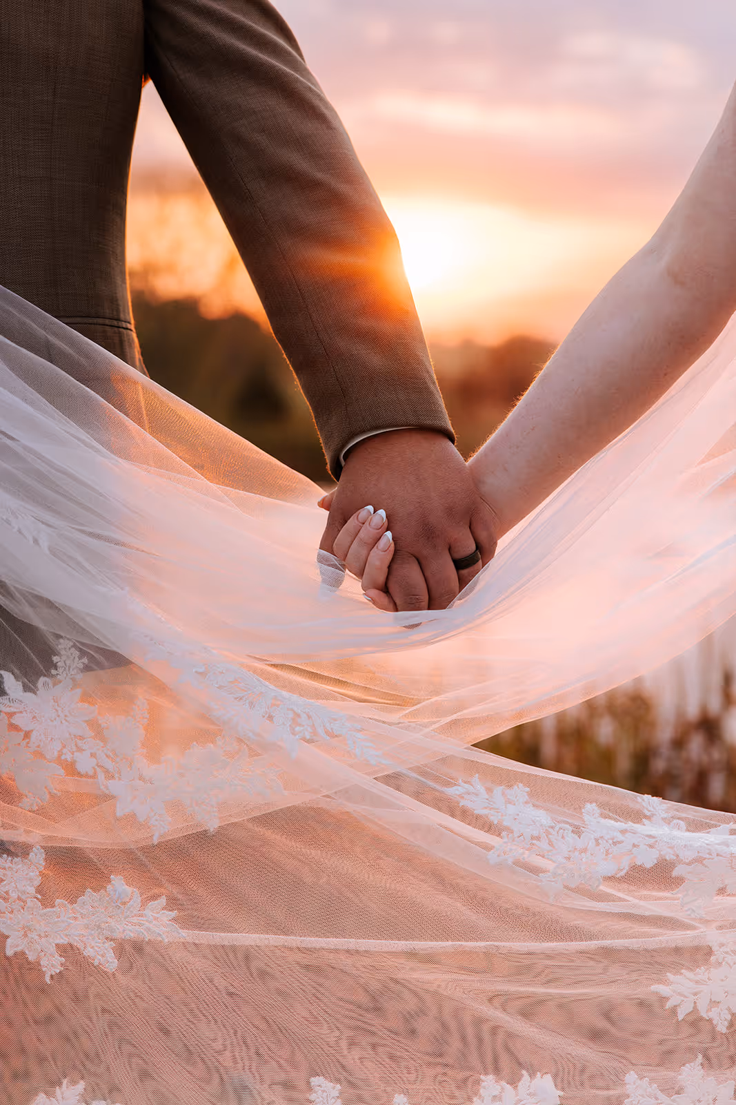 Hands intertwined with the bridal veil at sunset