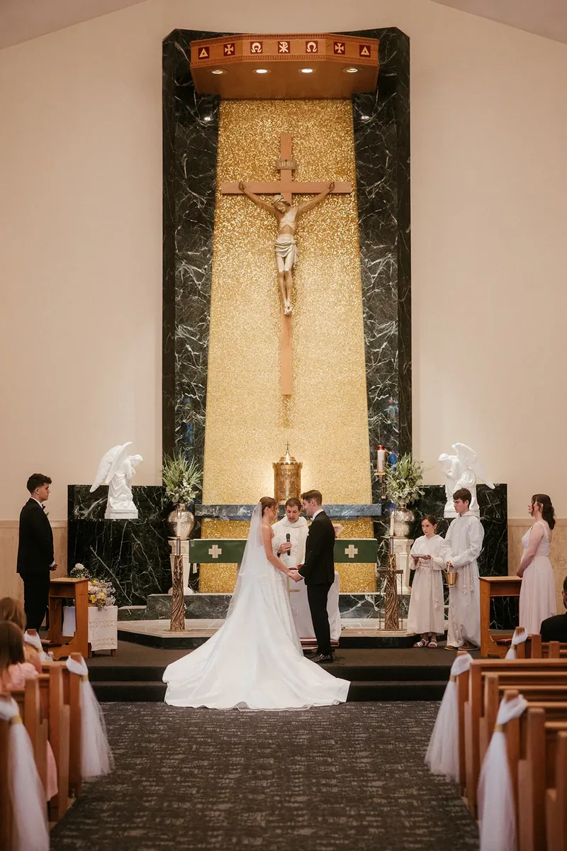 Bride and groom exchanging vows at a church altar beneath a crucifix