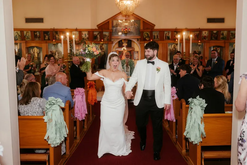 Newlyweds walking down the church aisle as guests applaud