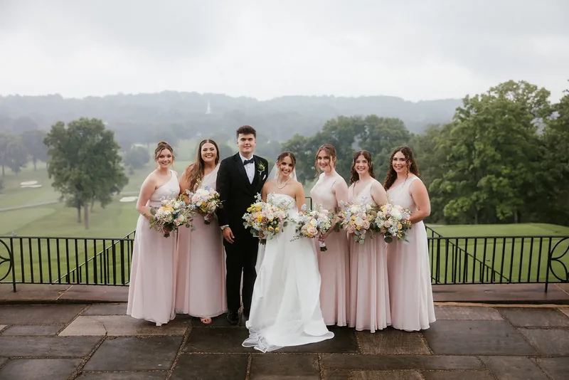 Bride with attendants in pale pink on a terrace overlooking a golf course