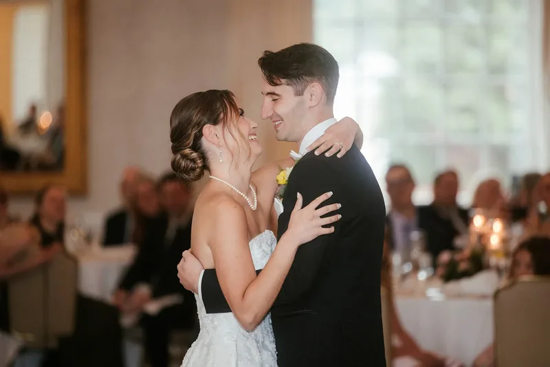 Bride and groom smiling during their first dance with guests behind them