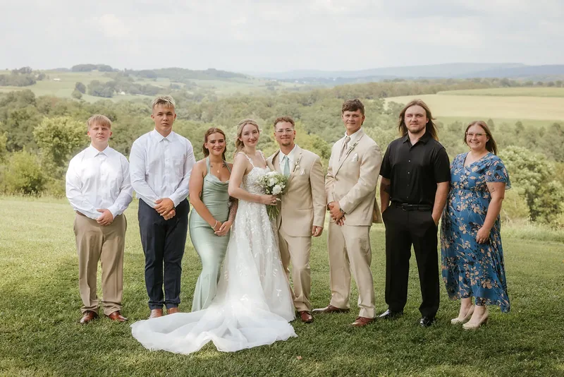 Newlyweds posing with a family group against the countryside.