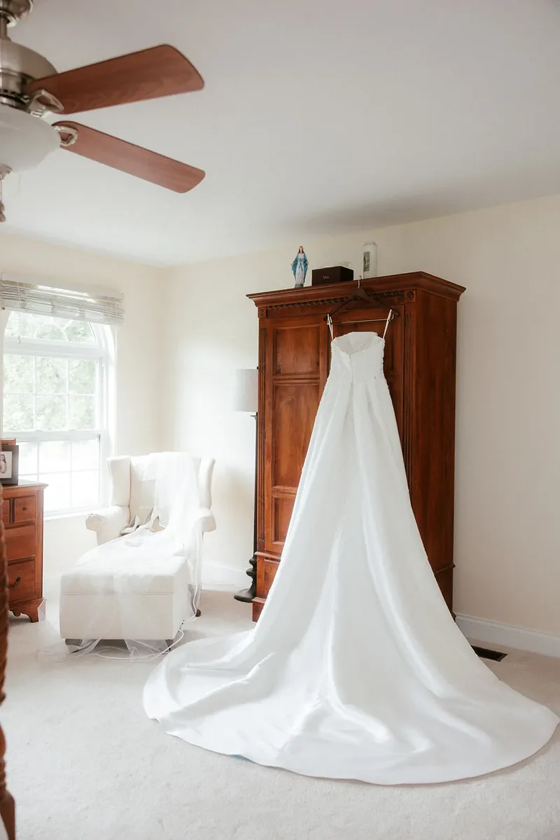 Strapless wedding dress and train hanging beside a bright window