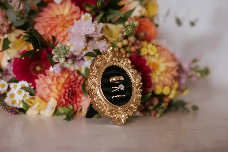 Wedding rings in an ornate gold frame against a colorful bridal bouquet