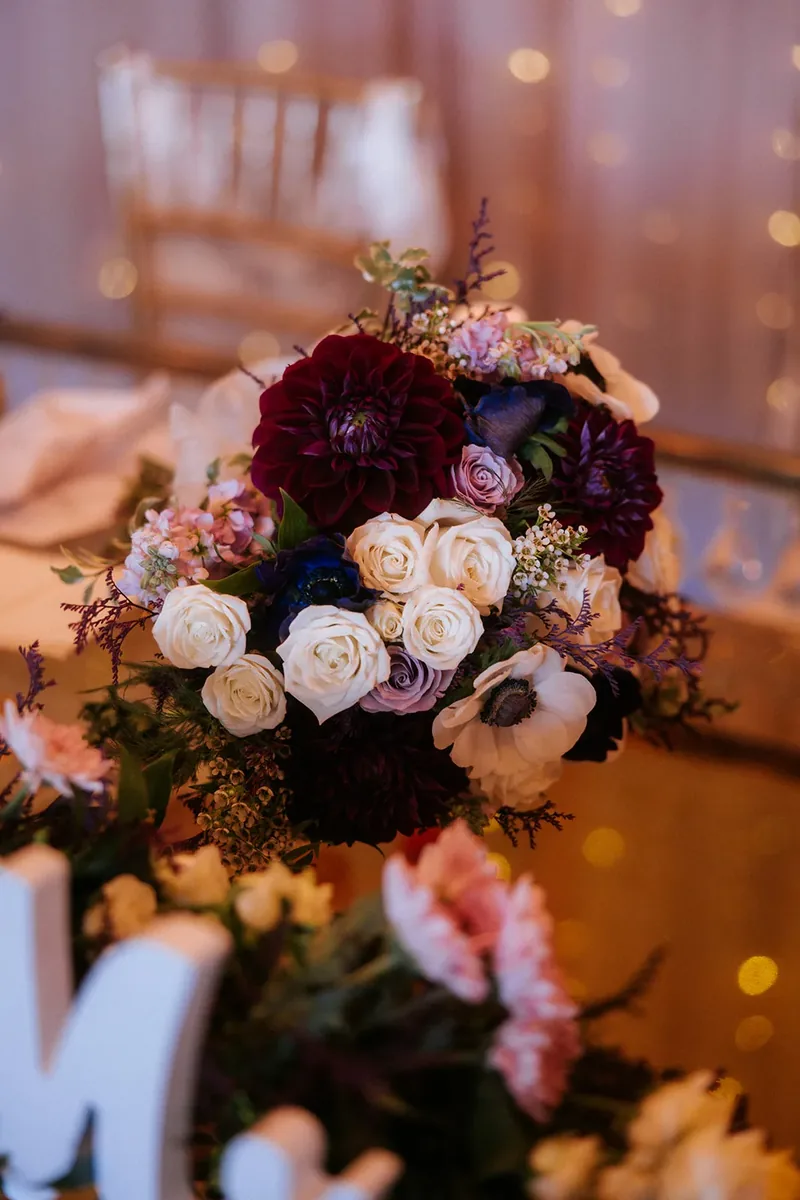 Burgundy, white and lavender bridal bouquet on a reception table.