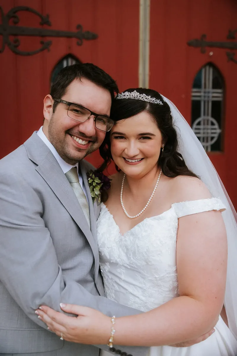 Newlyweds smiling together in front of red church doors.