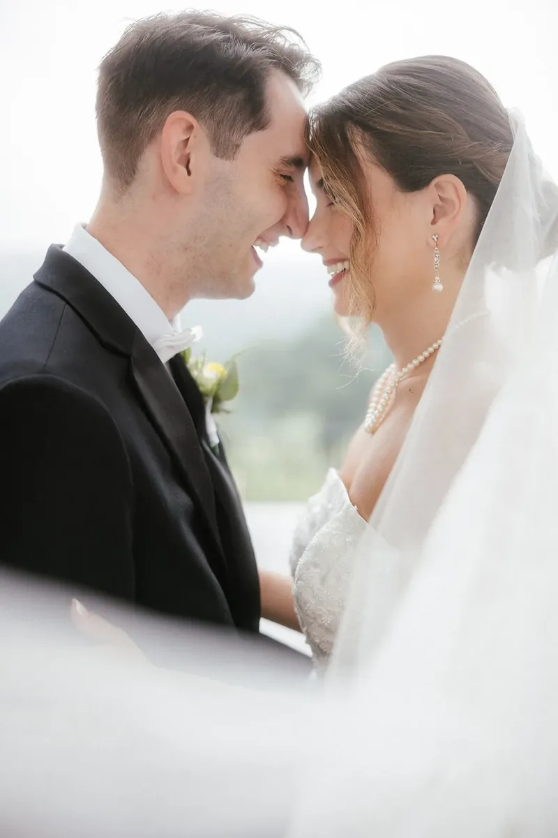 Bride and groom touching foreheads beneath a sheer wedding veil