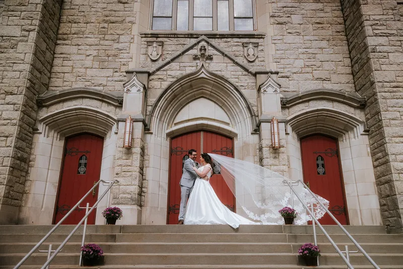 Bride and groom on the stone church steps with the veil flowing.