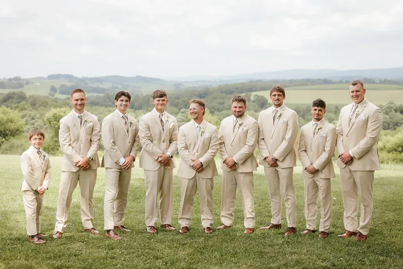Groom and groomsmen in tan suits overlooking rolling green hills.