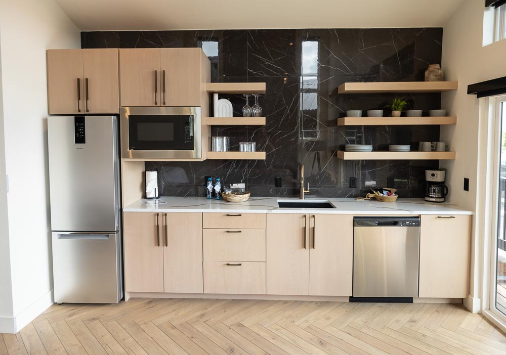 Suite kitchenette with stainless appliances, dark stone backsplash and floating wood shelves