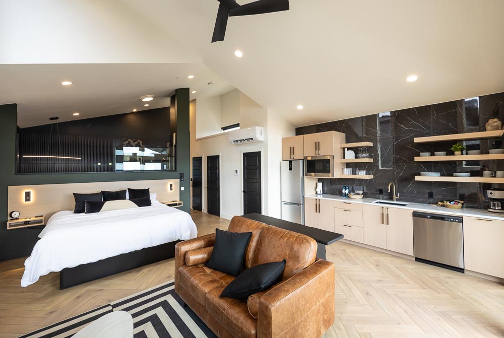 King bed and leather sofa in an open suite with a kitchenette behind