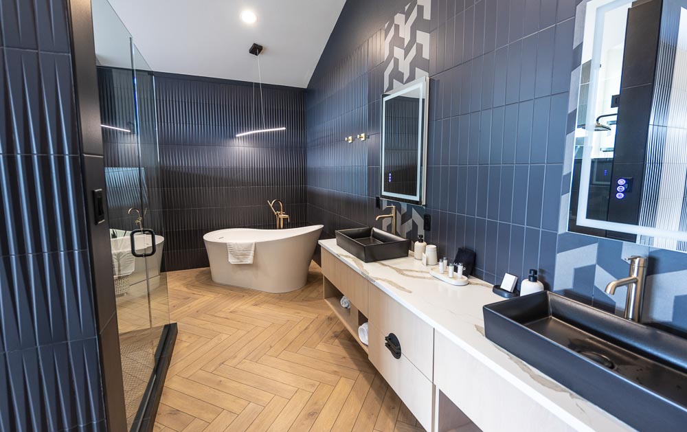 Bathroom with a freestanding soaking tub, double vanity and black tile walls