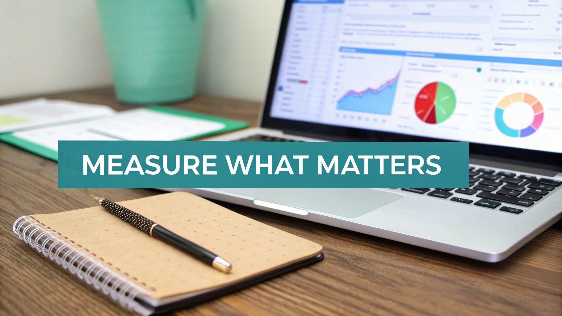 A business desk with a laptop showing analytics, a notebook, and a pen, featuring the text "MEASURE WHAT MATTERS."