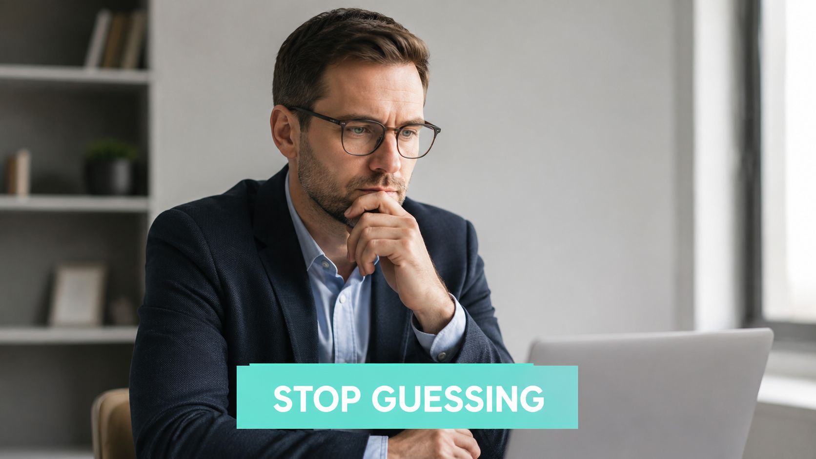 A professional man in a suit looking thoughtfully at his laptop screen while sitting at a desk.