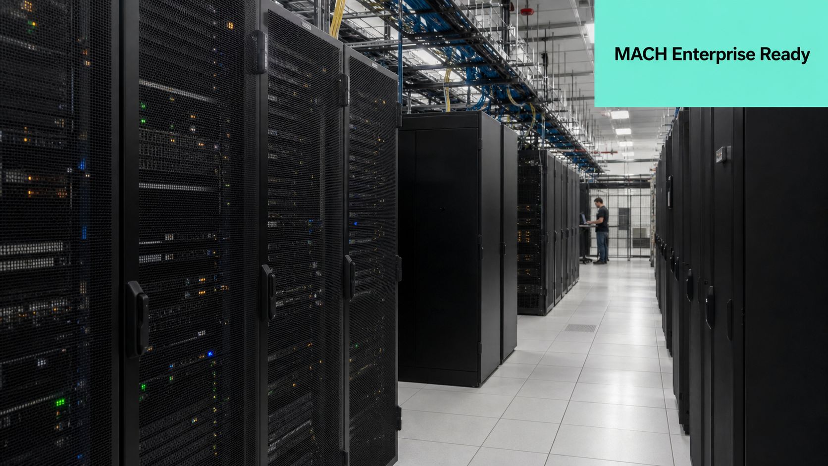 A rows of black server racks in a modern data center with an IT technician working nearby.