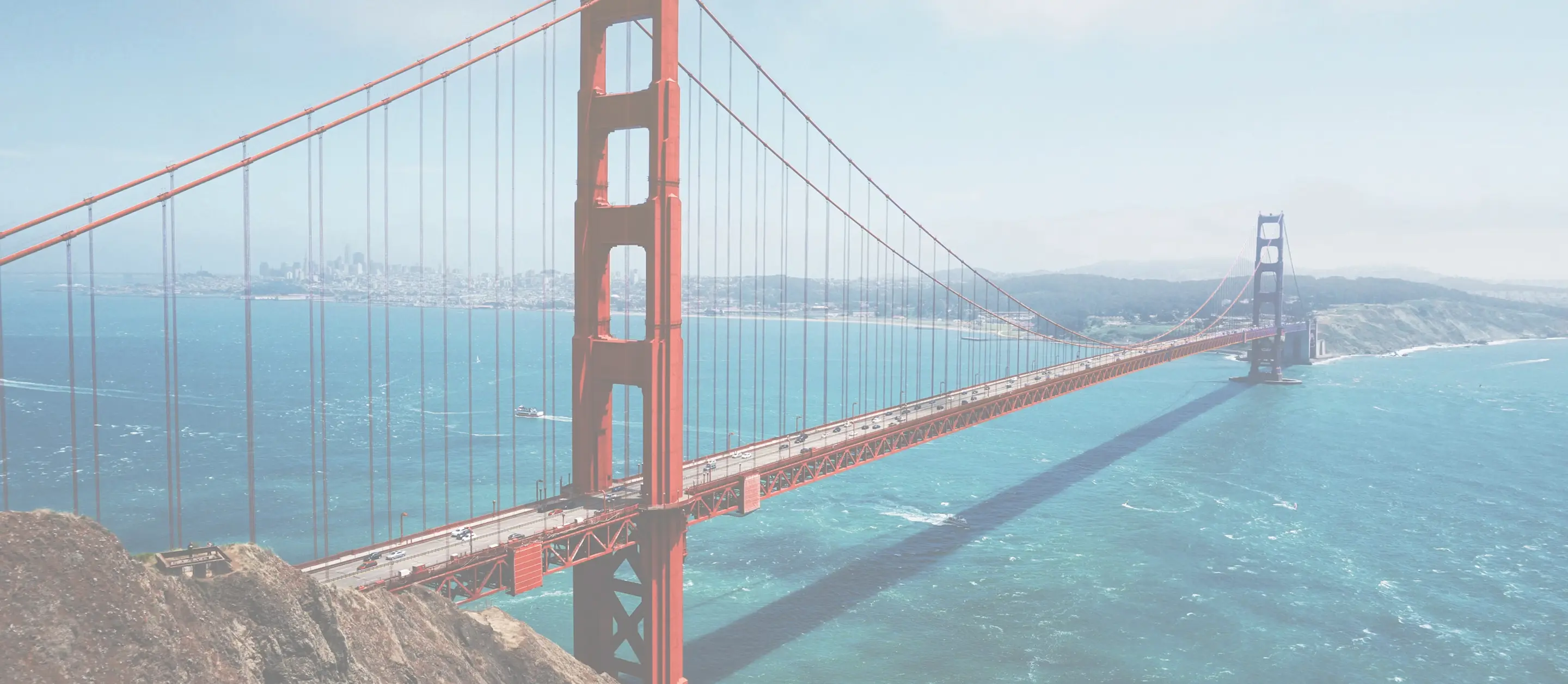 Golden Gate Bridge spanning blue water with city skyline and hills in the background.