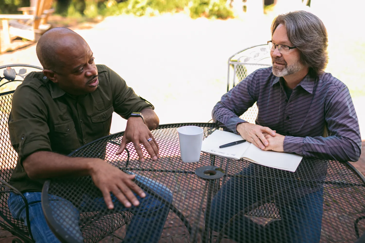 Chuck Coward (The Struggle Coach) seated at an outdoor patio table listening to another man speak.