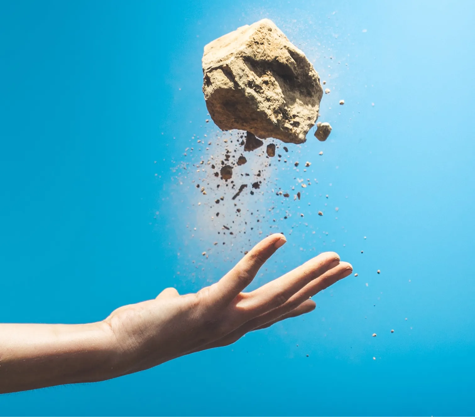 A human hand hurls a crumbling rock upward against a bright blue background.