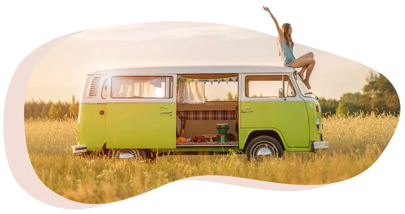 Une jeune femme blonde en short et débardeur est assise sur le toit d'un van rétro vert clair stationné dans un champ de blé sous un ciel clair.