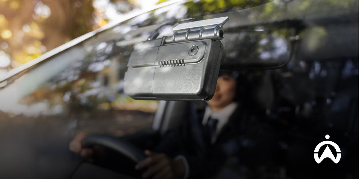 Cartrack truck camera system mounted on windshield, recording driver in suit with sunny view outside.