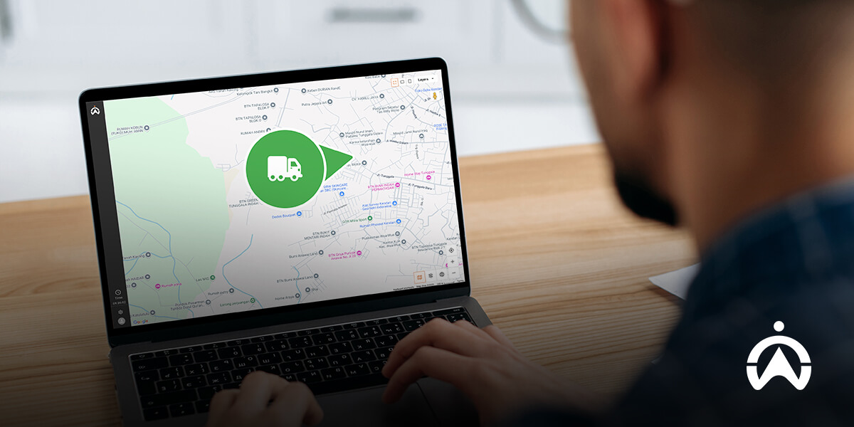 A person views a map on a laptop, featuring a green pin highlighting a truck's location, suggesting transportation or delivery tracking.