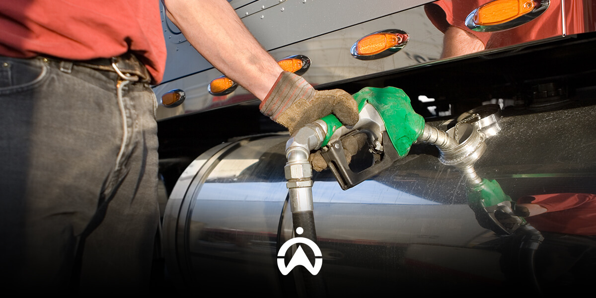 A person in gloves fills a truck's fuel tank with a green nozzle at a gas station, showcasing the fuel transfer process.