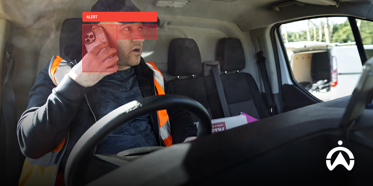A driver in an orange safety vest looks at their phone while seated in a vehicle, surrounded by a cluttered interior.