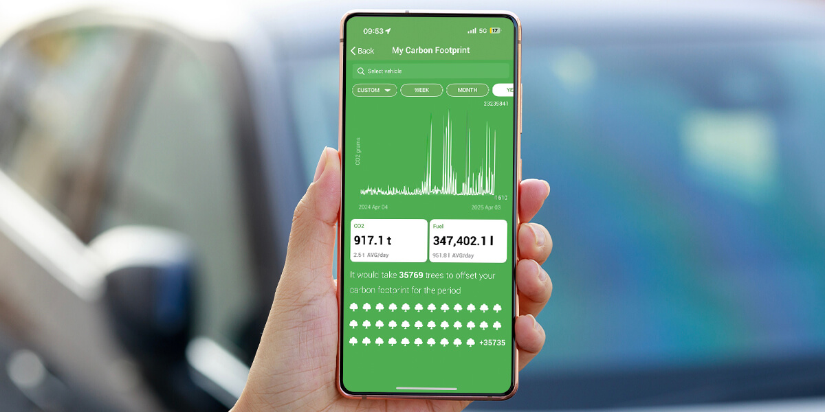 A hand holds a smartphone displaying carbon footprint data, including CO2 emissions and trees needed for offsetting, against a blurred car background.
